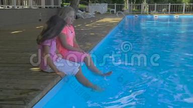 两个小女孩在游泳池里泡脚的户外镜头。 可爱的小女孩坐在游泳的边缘